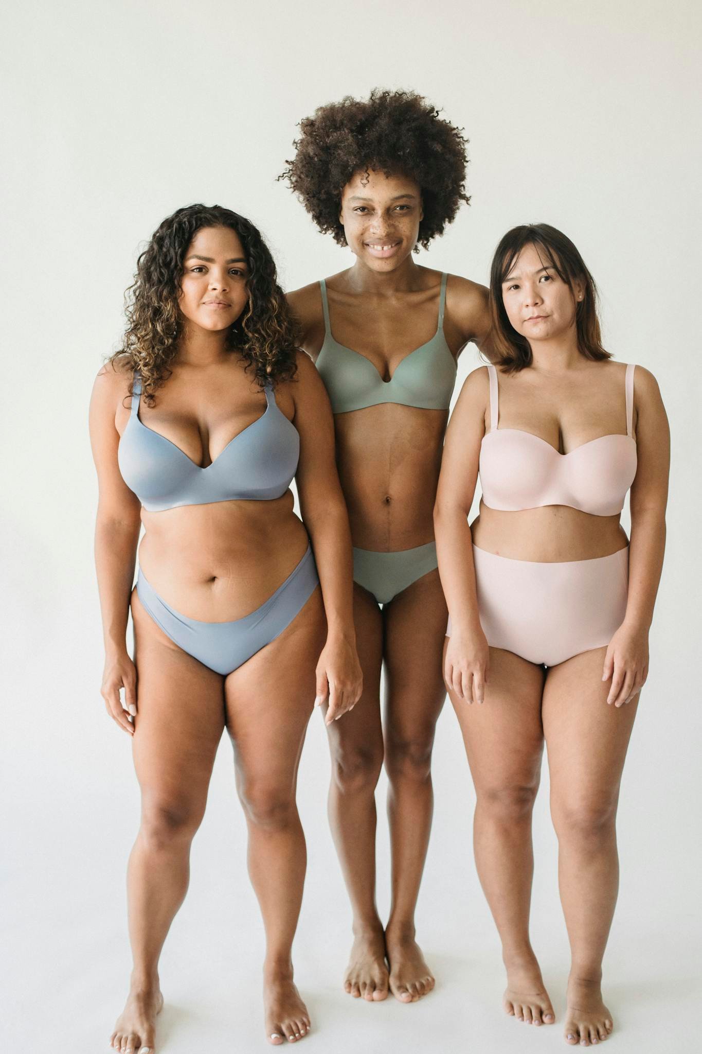 Celebrating body diversity with three women in pastel lingerie sets, expressing confidence.