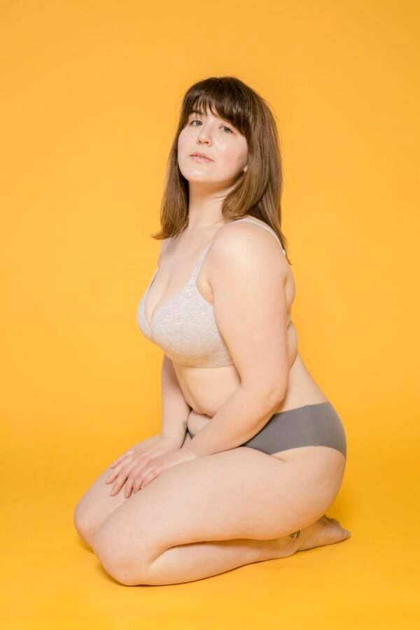 A confident plus size woman poses in lingerie against a vibrant yellow background.