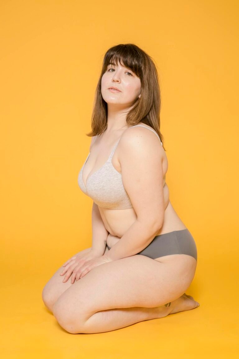 A confident plus size woman poses in lingerie against a vibrant yellow background.