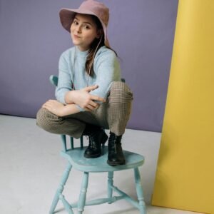 A young girl sitting playfully on a pastel blue chair, expressing joy and style.