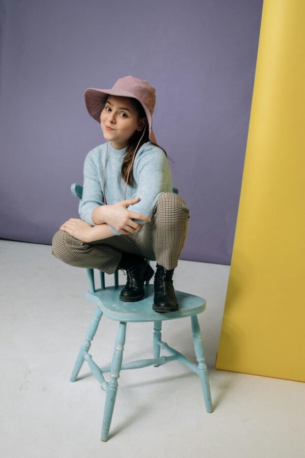 A young girl sitting playfully on a pastel blue chair, expressing joy and style.