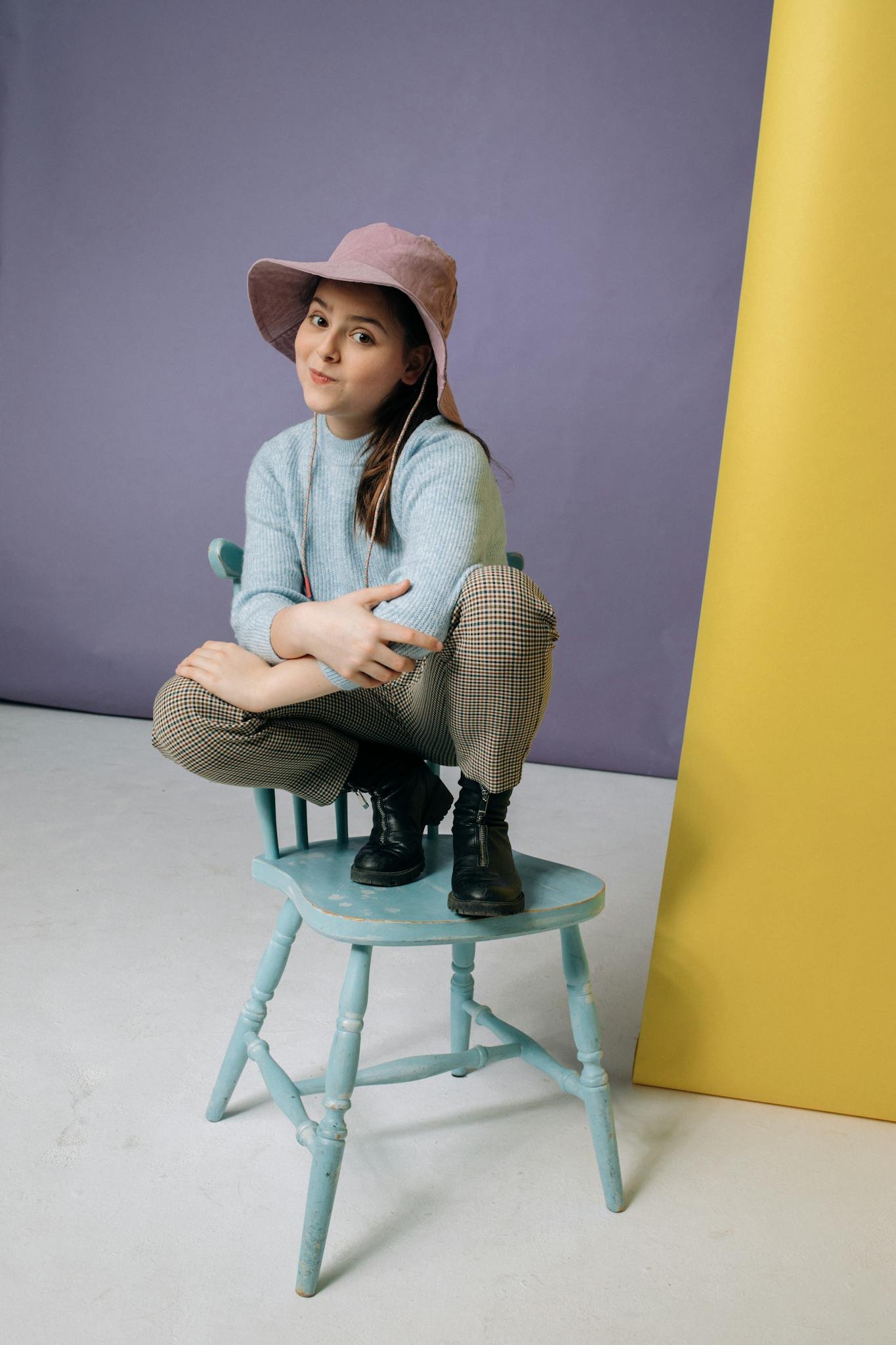 A young girl sitting playfully on a pastel blue chair, expressing joy and style.