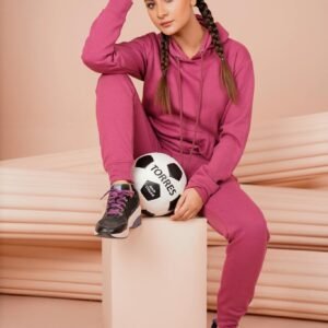 Confident young female in pink athletic wear holding a soccer ball indoors.