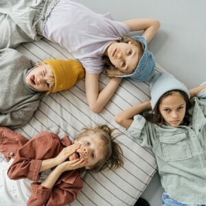 Group of four children in fashionable attire lying on a striped blanket, expressing playfulness and style.