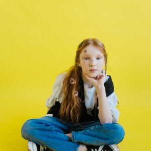 Young girl sitting casually on a vibrant yellow background with fun facial stickers.