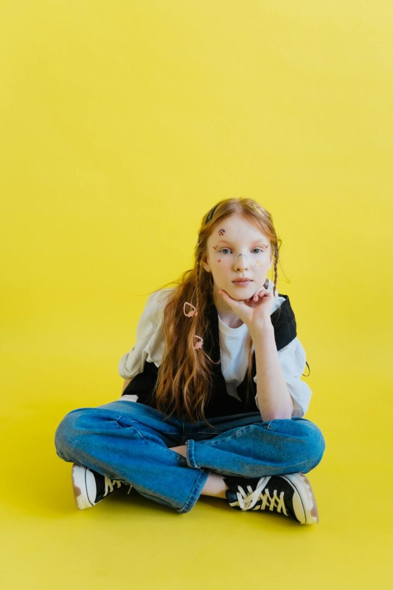 Young girl sitting casually on a vibrant yellow background with fun facial stickers.